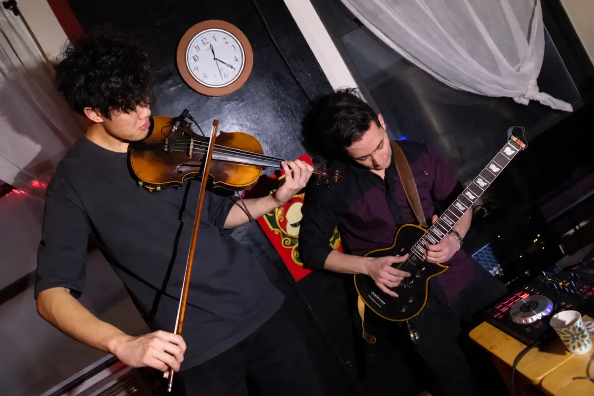 A violinist and guitarist playing together beside a DJ setup