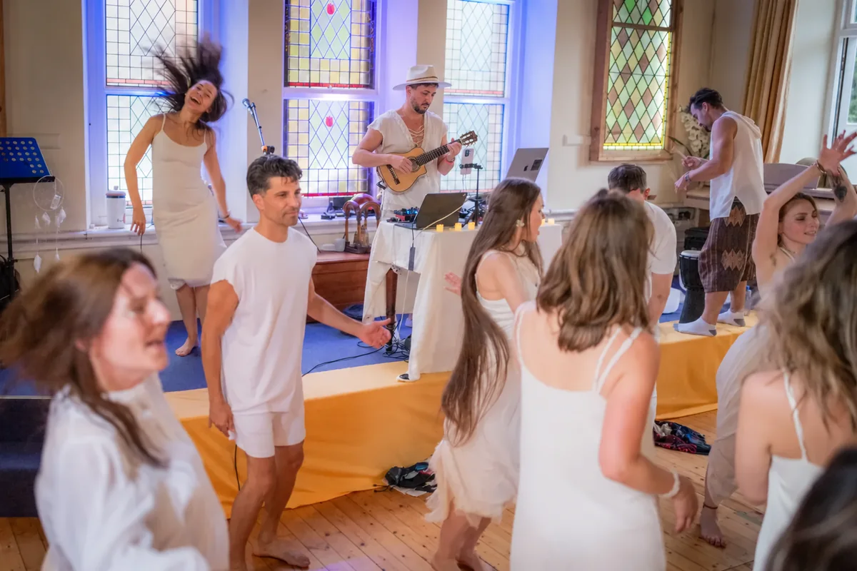 Sasha, wearing a beige hat, playing guitar as dancers dressed in white move around him